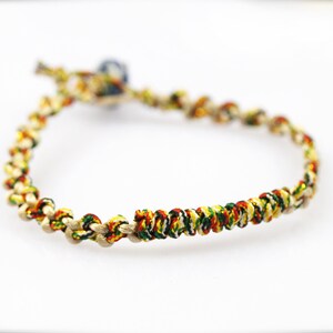 May include: A braided bracelet with red, yellow, green, and gold threads. The bracelet has a small blue bead at the end.