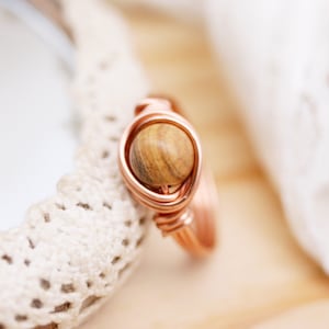 Könnte beinhalten: Ein Ring aus Kupferdraht mit einer braunen Holzperle in der Mitte.