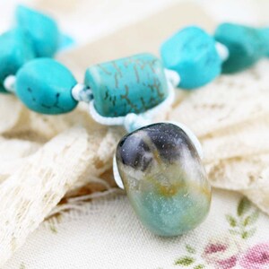 Peut inclure: Un collier de pierres précieuses turquoise et vertes avec un grand pendentif en pierre précieuse vert et brun de forme irrégulière. Le collier est composé de perles turquoise et d'une perle turquoise en forme de tonneau avec des marques dorées.