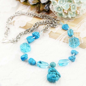 Puede incluir: Un collar de piedras preciosas turquesa y azul claro con una cadena de plata. El collar presenta un gran colgante turquesa.