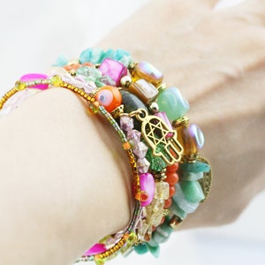 May include: A stack of colorful bracelets with various beads, including turquoise, pink, orange, and gold. The bracelets feature a hamsa hand charm and an evil eye bead.