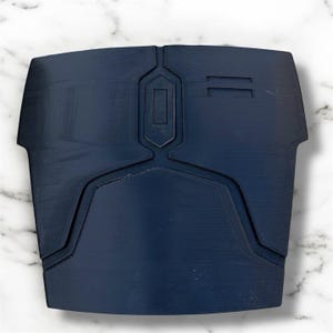 May include: A navy blue chest plate with geometric designs. The plate has a central rectangular design and two parallel lines on the right side. The edges have a curved shape. The item is likely a piece of armour or cosplay.