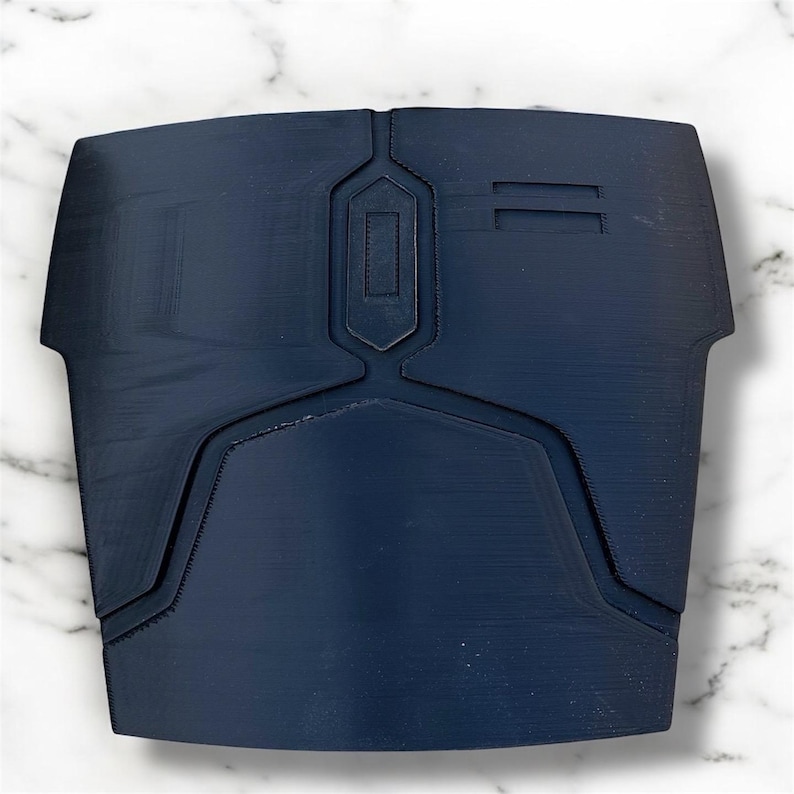 May include: A navy blue chest plate with geometric designs. The plate has a central rectangular design and two parallel lines on the right side. The edges have a curved shape. The item is likely a piece of armour or cosplay.