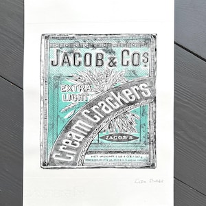 May include: A black and white print of a vintage Jacob & Co. Cream Crackers box. The design features the brand name, product name, and wheat stalks, with a teal and black color scheme. The net weight is 507g.