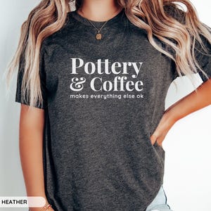 May include: A dark grey heather t-shirt with the text "Pottery & Coffee makes everything else ok" printed in white.