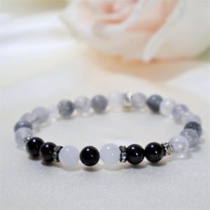 May include: A bracelet with white and black beads. The bracelet is made of clear quartz, black onyx, and white jade. The beads are separated by silver spacers.