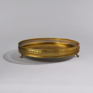 May include: A gold-toned metal serving tray with a decorative, openwork rim and three feet. The tray has a round shape and a smooth surface.
