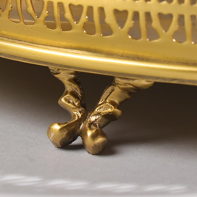 May include: A gold metal decorative stand with a round top and three ornate legs. The stand has a delicate, intricate design.