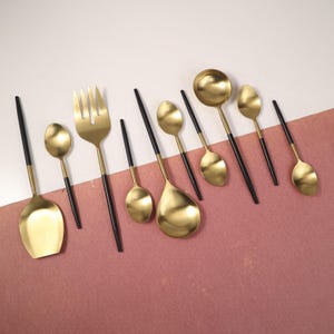 May include: A set of gold-coloured flatware with black handles. The set includes a fork, a spoon, and a ladle.