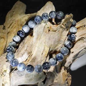 Könnte beinhalten: Ein Armband aus runden, grauen und weißen Edelsteinperlen. Die Perlen haben eine wolkig-marmorierte Optik.