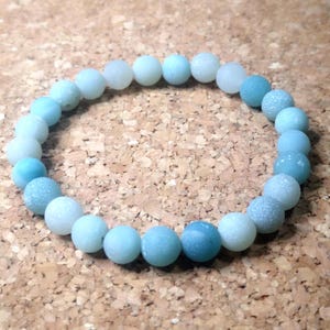 Könnte beinhalten: Ein hellblaues Ombre-Perlenarmband mit mattem Finish. Die Perlen sind rund und in der Größe abgestuft, wodurch ein subtiler Ombre-Effekt entsteht.
