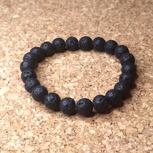 Könnte beinhalten: Ein schwarzes Armband aus Lavasteinen. Das Armband besteht aus kleinen, runden Perlen mit einer rauen, strukturierten Oberfläche.