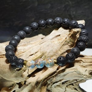 Könnte beinhalten: Ein schwarzes Armband aus Lavastein mit drei blauen und braunen Jaspisperlen und goldenen Zwischenstücken.