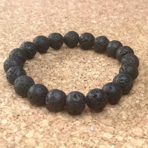 Op de afbeelding: Een zwarte armband van lavastenen kralen. De kralen zijn rond en hebben een ruw, getextureerd oppervlak.