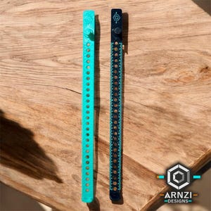 May include: Two measuring tapes, one black and one turquoise, with a white logo on the black tape. The tapes are made of plastic and have a series of holes along the length. The tapes are on a wooden surface.