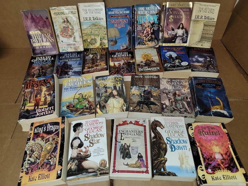 May include: A collection of fantasy and science fiction paperback books with various covers featuring dragons, wizards, and other mythical creatures. The books are arranged in a grid pattern on a brown surface.