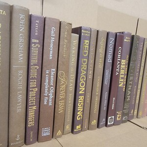 Pu&ograve; includere: Una collezione di libri con copertina rigida con vari titoli e autori. I dorsi sono in tonalit&agrave; di marrone, beige e viola, con scritte dorate. I titoli includono "Darwin's Backyard", "Rogue Lawyer" e "Red Dragon Rising."