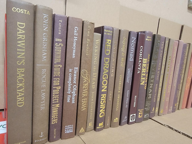 Pu&ograve; includere: Una collezione di libri con copertina rigida con vari titoli e autori. I dorsi sono in tonalit&agrave; di marrone, beige e viola, con scritte dorate. I titoli includono "Darwin's Backyard", "Rogue Lawyer" e "Red Dragon Rising."