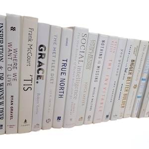 Pu&ograve; includere: Una collezione di libri con copertina rigida e dorso bianco, disposti su uno scaffale. I titoli includono "Storm Surge", "Inspiration", "Where We Want to Live" e "Grace". I libri sono di varie dimensioni e caratteri.