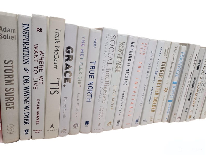 Pu&ograve; includere: Una collezione di libri con copertina rigida e dorso bianco, disposti su uno scaffale. I titoli includono "Storm Surge", "Inspiration", "Where We Want to Live" e "Grace". I libri sono di varie dimensioni e caratteri.