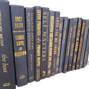 May include: A collection of black hardcover books with gold lettering on the spines. The books are arranged in a row, with the spines facing the viewer. The titles of the books include "Seven Promises of a Promise Keeper", "Self Matters", "Developing the Leader Within You", "Look for Me There", "The Gift of Forgiveness", "Artificial You", "Saved by a Song", "Not Giving a F*ck", "Love Must Be Tough", "Manson", "Invisible God", "Rainet", "Three Days in Moscow", "Galileo and the Science Deniers", "Bret Baier", "Stephenie Meyer, the host".