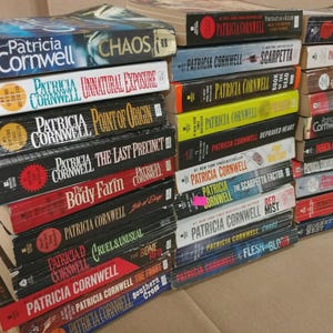 May include: A collection of Patricia Cornwell books, featuring titles like "Chaos," "Unnatural Exposure," and "Point of Origin." The books have various colored spines and covers, with the author's name prominently displayed. The books are stacked in a pile.