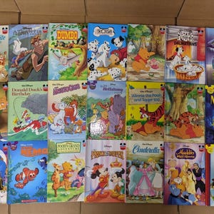 May include: A collection of Disney storybooks featuring various animated films. Titles include "Snow White," "Dumbo," "The Little Mermaid," "Toy Story 3," and others. The books have colorful illustrations and are arranged in rows.