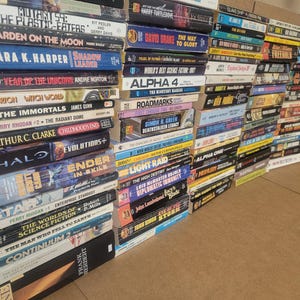 May include: A stack of paperback books with science fiction and fantasy titles. The books are arranged in a vertical stack, with the spines facing out. The titles include "Mutant 59: The Plastic-Eaters", "Garden on the Moon", "Shadow Leader", "Year of the Unicorn", "The Immortals", "Childhoood's End", "Halo", "Ender in Exile", "Star", "The Worlds of Science Fiction", "The Man Who Fell to Earth", "Continuum 2", "David Drake: The Way to Glory", "World's Best Science Fiction", "Alpha 4", "Roadmarks", "Simon & Green: Beatstalker Legacy", "Light Raid", "The High Destiny: Diplomatic Immunity", "John Ringo:  Eye of the Storm", "Alpha One", "Freeworld", "Frank Herbert:  Dune".