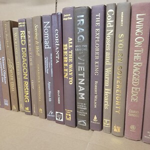 Pu&ograve; includere: Una collezione di libri con copertina rigida con vari titoli e autori. I dorsi sono in tonalit&agrave; di marrone, grigio e viola, con lettere dorate o bianche. I libri sono disposti in fila, suggerendo una biblioteca o una libreria.