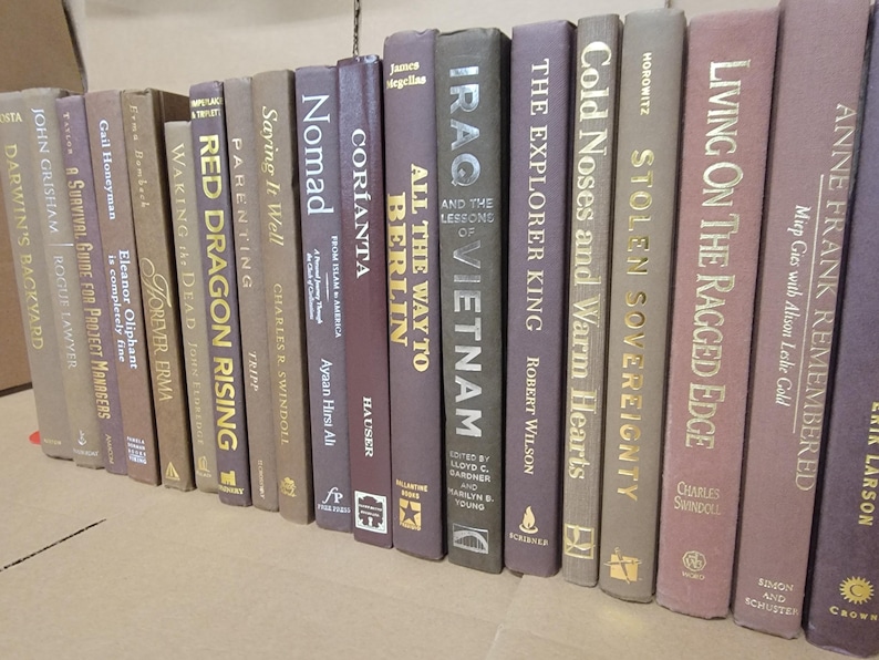 Pu&ograve; includere: Una collezione di libri con copertina rigida con vari titoli e autori. I dorsi sono in tonalit&agrave; di marrone, grigio e viola, con lettere dorate o bianche. I libri sono disposti in fila, suggerendo una biblioteca o una libreria.