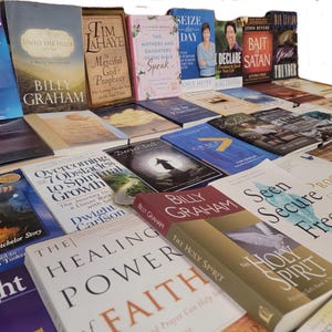 May include: A collection of various Christian books and novels stacked on top of each other. The books have different titles and authors, including "Seize the Day", "Bait and Declare Satan", "The Mothers and Daughters of the Bible Speak", "Unto the Hills", "Merciful God Prophecy", "Overcoming 7 Obstacles to Spiritual Growth", "The Healing Power of Faith", "The Holy Spirit", "Seen Secure Free", "Proof of Heaven", and "Billy Graham".