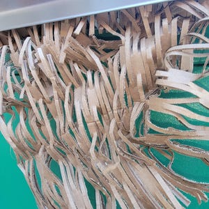 May include: Close-up of a brown paper shredder with shredded paper hanging down in front of a green background.