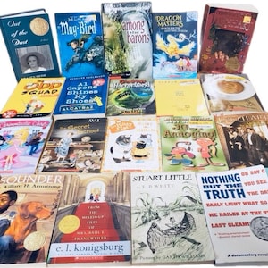 May include: A collection of 20 paperback books, mostly for young adults, with a variety of genres and authors. The books are stacked in a pyramid shape, with the titles facing outward. Some of the titles include "Out of the Dust", "Mag Bird", "Among the Barons", "Dragon Masters", "The Odd Squad", "Al Capone Shines My Shoes", "The Secret School", "3D Annoying", "Sounder", "From the Mixed-Up Files of Mrs. Basil E. Frankweiler", "Stuart Little", "Nothing But the Truth", "On Say Can You See", "Call It Courage".