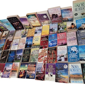 May include: A collection of Nora Roberts novels, featuring various book covers with titles like "Irish Born," "Montana Sky," and "Danger Zone." The books are arranged in a display, showcasing a variety of colors and designs.