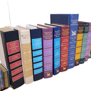 May include: A collection of 14 hardcover books with colorful spines. The books are arranged vertically in a row. The books are all Reader's Digest Condensed Books. The titles of the books are visible on the spines. The books are in various colors, including red, blue, green, purple, and yellow.