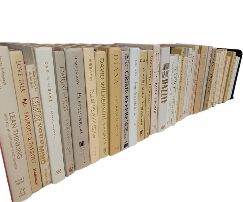 Pu&ograve; includere: Una collezione di libri con copertina rigida con vari titoli e autori. I dorsi sono principalmente color crema, beige e bianco sporco, con titoli come "Love Talk", "Exercise Your Mind" e "Crime Reference". I libri sono disposti in una fila leggermente curva.