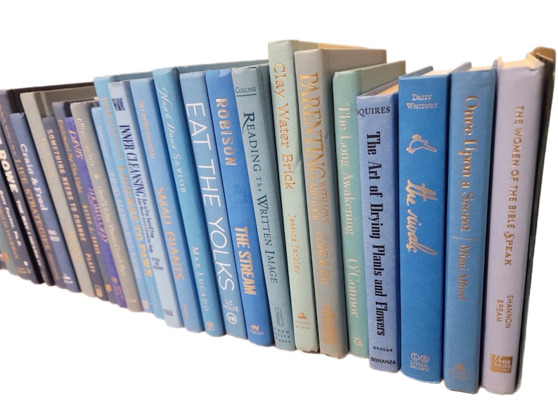 Pu&ograve; includere: Una collezione di libri con copertina rigida in varie tonalit&agrave; di blu, grigio e verde. I dorsi mostrano titoli in lettere dorate. I libri sono disposti ad angolo, creando un'esposizione visivamente accattivante.