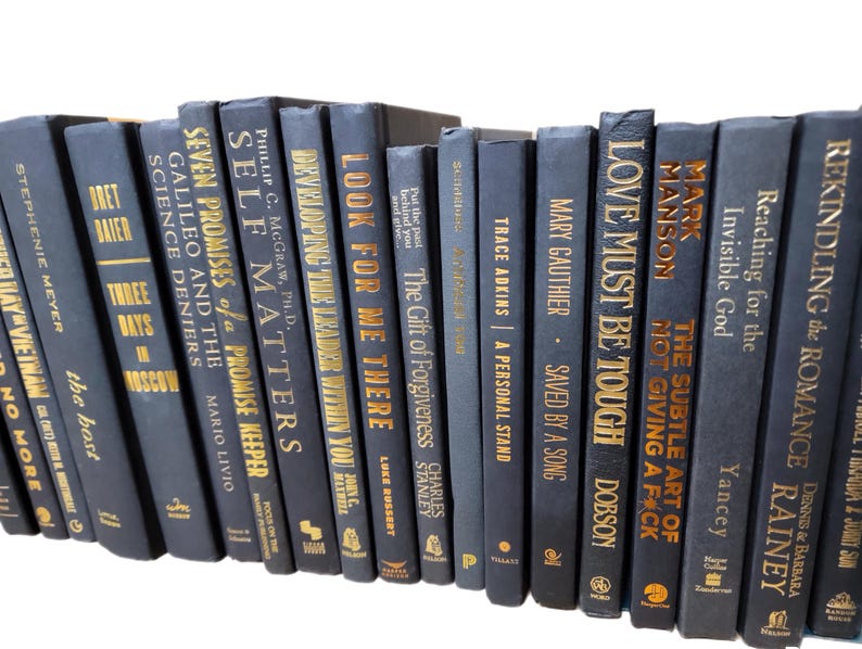May include: A collection of 20 navy blue hardcover books with gold lettering on the spines. The books are arranged vertically in a row. The titles of the books include "Love Must Be Tough", "The Subtle Art of Not Giving a F*ck", "Self Matters", "Developing the Leader Within You", "Look for Me There", "Seven Promises of a Promise Keeper", "Galileo and the Science Deniers", "Three Days in Moscow", "The Gift of Forgiveness", "Reaching for the Invisible God", "Rekindling the Romance", and more.
