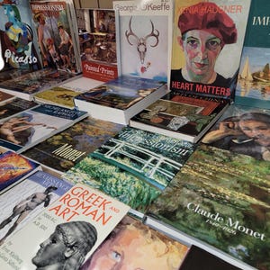 May include: A collection of art books featuring various artists, including Picasso, Turner, Monet, and Claude Monet. The books are arranged in a pile on a table, with the spines facing outward. The titles of the books are visible, as well as the names of the artists.