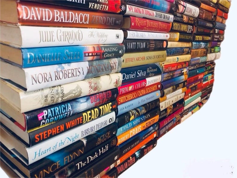 May include: A stack of paperback books with various titles and authors. The books are arranged in a staggered pattern, with the top of the stack leaning to the right. The books are all different colors and have different designs on their covers.