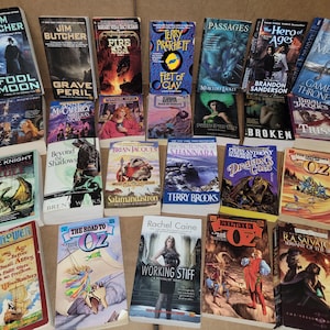 May include: A collection of fantasy and science fiction paperback books with various titles and authors. The books are arranged in a grid pattern on a brown surface.