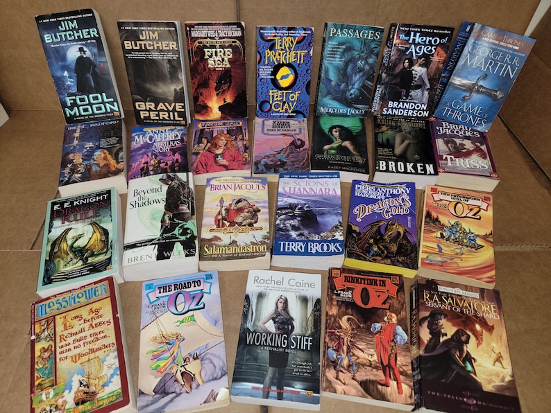 May include: A collection of fantasy and science fiction paperback books with various titles and authors. The books are arranged in a grid pattern on a brown surface.