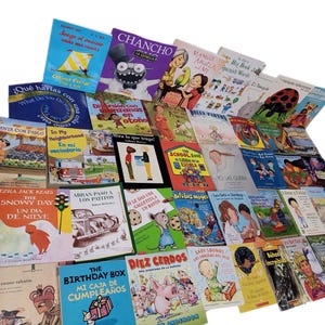 May include: A collection of colorful children's books in Spanish and English, featuring various themes such as animals, food, and learning. The books are arranged in a pile, with some titles visible, including "Chancho", "Mango", "Abulá", and "The Snowy Day".