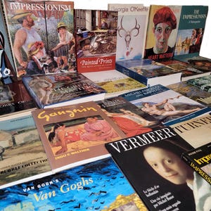 May include: A stack of art books featuring various artists, including Picasso, Impressionists, Georgia O'Keeffe, and Vermeer. The books are arranged in a staggered pattern, with the titles and authors visible.