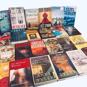 May include: A collection of paperback books stacked in a pyramid shape. The books are mostly fiction and include titles like "The Kite Runner", "Lost Symbol", "The Chase", "Victims", "The Amateur Marriage", and "The Woman Next Door".