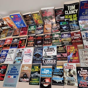 May include: A large collection of paperback books by Tom Clancy, featuring titles such as "Dead or Alive", "Airborne", "Patriot Games", "The Hunt for Red October", and "Fighter Wing".