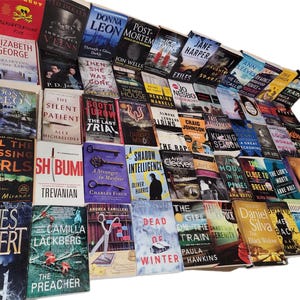 May include: A large collection of paperback books with various titles and authors. The books are stacked in a pile, with the spines facing out. The books are mostly in the mystery and thriller genres.