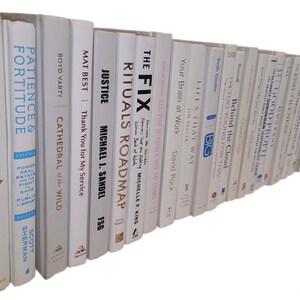 Pu&ograve; includere: Una collezione di libri con copertina rigida bianca con titoli visibili sul dorso. I titoli includono "The Awakened Family", "Patience & Fortitude" e "Justice". I libri sono disposti su una mensola.