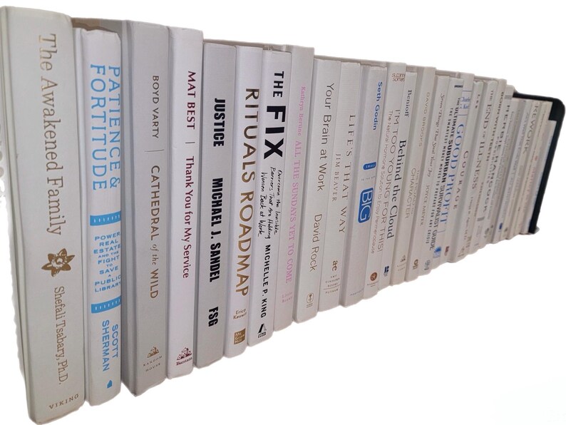 Pu&ograve; includere: Una collezione di libri con copertina rigida bianca con titoli visibili sul dorso. I titoli includono "The Awakened Family", "Patience & Fortitude" e "Justice". I libri sono disposti su una mensola.