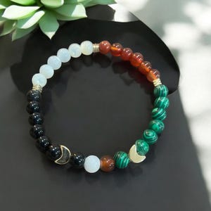 May include: A bracelet made of black, white, green, and brown beads with gold crescent moon charms.
